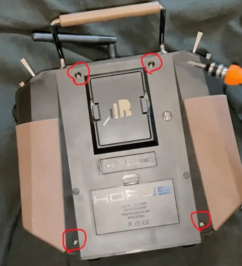 A remote control device (FrSky Horus X10S Express), for an FPV drone, is meticulously marked with four red circles, drawing attention to the screws. that has to be removed 
