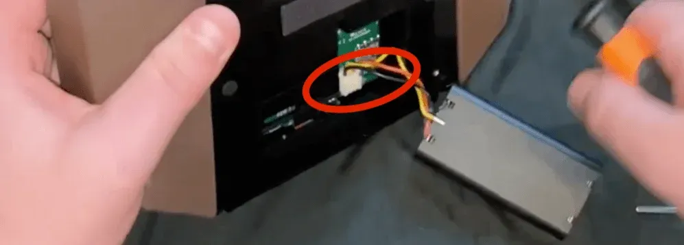 A pair of hands engages in precise work on an electronic device, with a red circle highlighting a key area of focus, in this case to remove the battery from the remote controller

